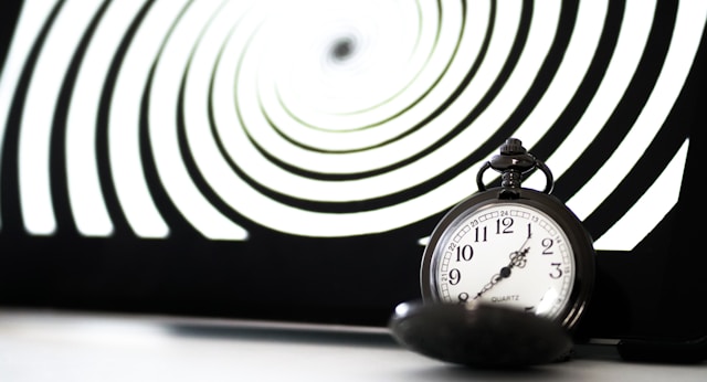 Otwarty srebrny zegarek kieszonkowy, a w tle widać czarno-białą spiralę